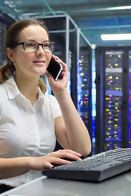 Frau telefoniert und tippt an PC in einem Rechenzentrum.