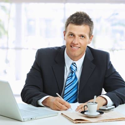 Webdesigner arbeitet am Schreibtisch mit Laptop und Kaffeetasse an einer Firmenhomepage.