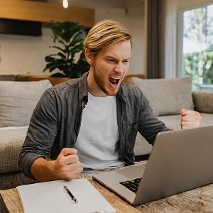 Wütender Mann im Wohnzimmer am Laptop.